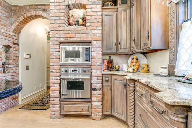 kitchen featuring appliances with stainless steel finishes, light stone counters, tasteful backsplash, light hardwood / wood-style floors, and brick wall