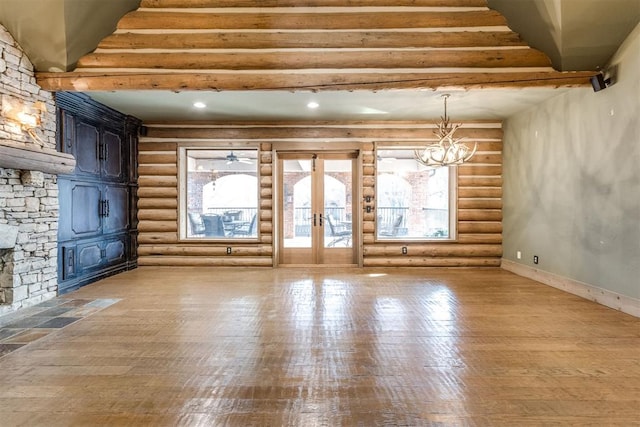 unfurnished living room featuring rustic walls, light hardwood / wood-style flooring, a notable chandelier, and french doors