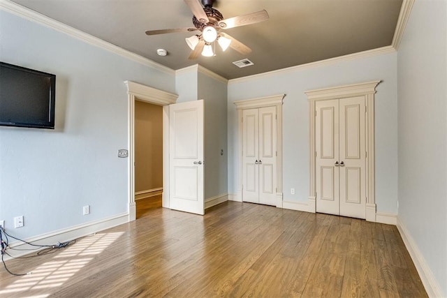 unfurnished bedroom featuring multiple closets, ceiling fan, ornamental molding, and hardwood / wood-style flooring