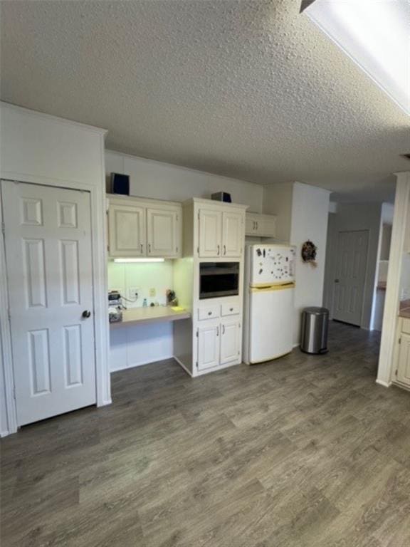 kitchen featuring black microwave, white refrigerator, wood-type flooring, a textured ceiling, and white cabinets