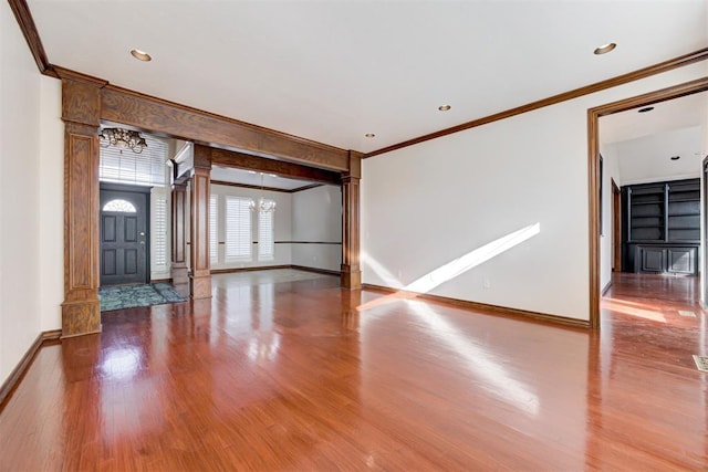 unfurnished living room with hardwood / wood-style floors, decorative columns, an inviting chandelier, and ornamental molding