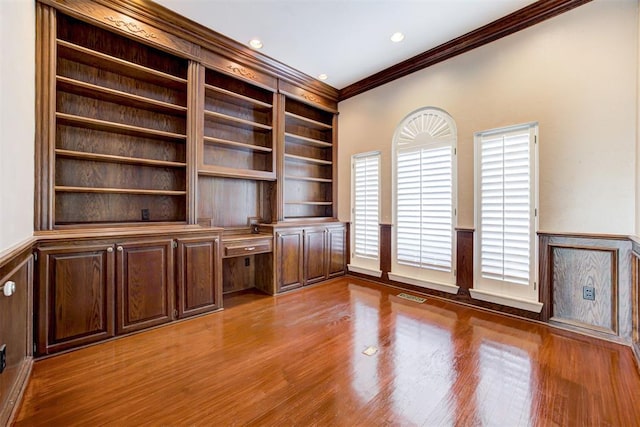 unfurnished office featuring ornamental molding, built in desk, and wood-type flooring