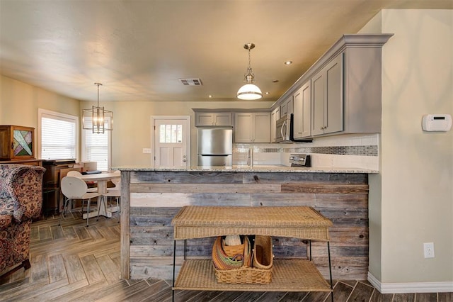 kitchen with decorative light fixtures, gray cabinets, light stone counters, and stainless steel appliances