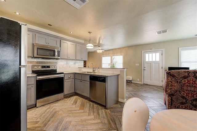 kitchen with gray cabinetry, sink, kitchen peninsula, decorative light fixtures, and appliances with stainless steel finishes