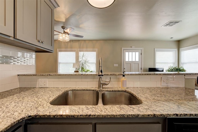 kitchen featuring backsplash, light stone countertops, sink, and a wealth of natural light