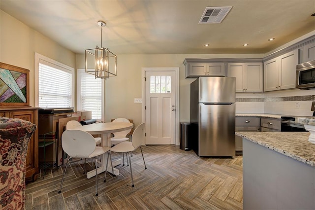 kitchen with light stone countertops, appliances with stainless steel finishes, parquet flooring, pendant lighting, and gray cabinets