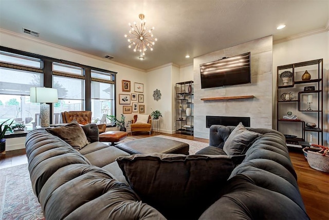 living room with hardwood / wood-style flooring, a large fireplace, crown molding, and an inviting chandelier