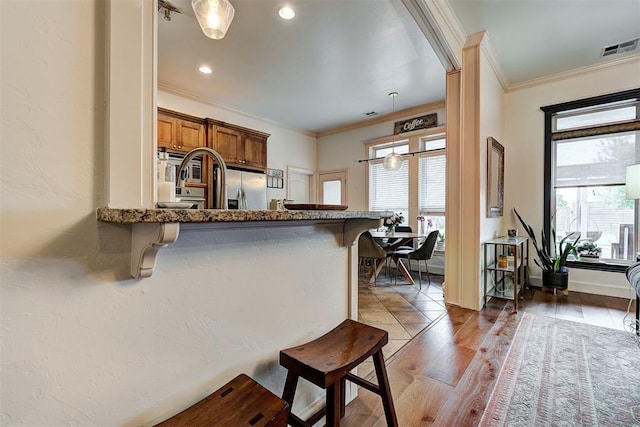 kitchen featuring stainless steel fridge with ice dispenser, crown molding, hanging light fixtures, and a breakfast bar area