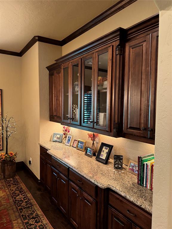 bar featuring light stone counters, dark brown cabinets, dark wood-type flooring, and ornamental molding