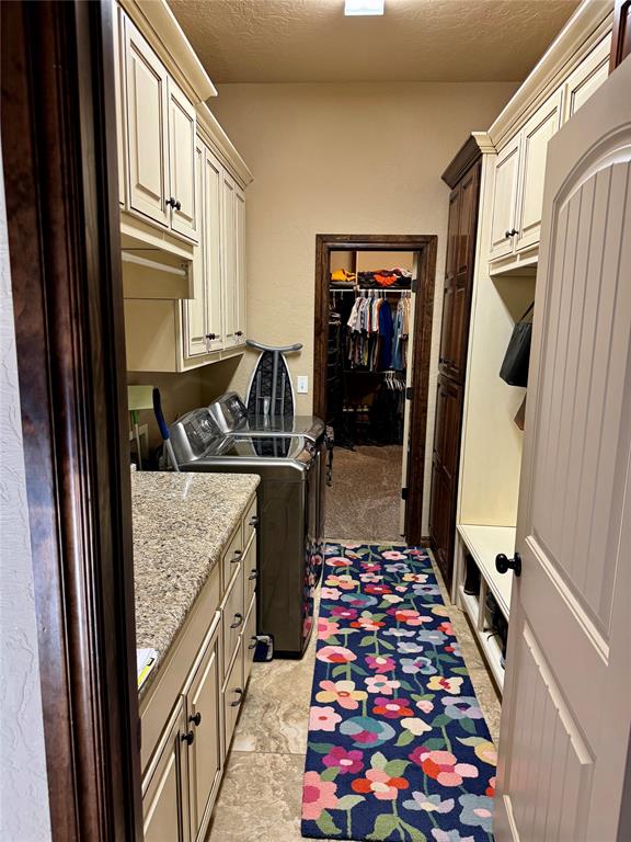 laundry room with light carpet, washer and clothes dryer, cabinets, and a textured ceiling