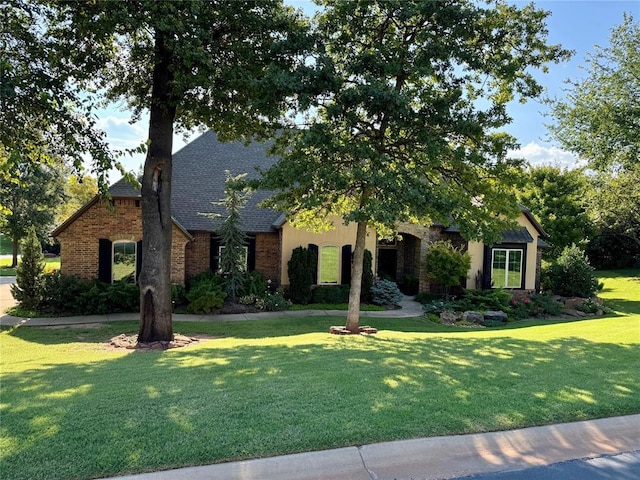 view of front facade with brick siding, a front yard, and roof with shingles