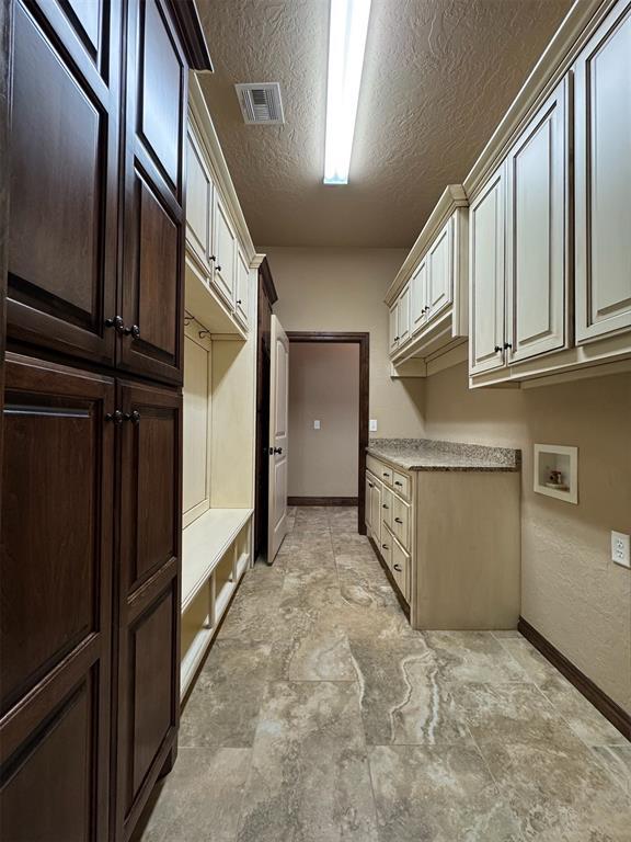 laundry area with visible vents, baseboards, hookup for a washing machine, cabinet space, and a textured ceiling