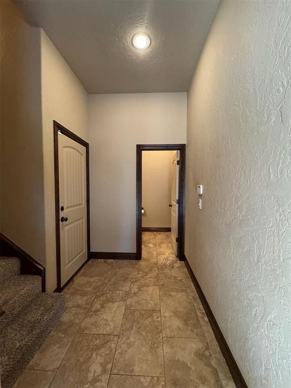 hallway featuring a textured ceiling, stairs, baseboards, and a textured wall