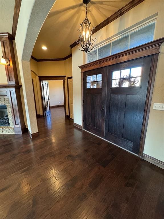 foyer featuring baseboards, a fireplace, arched walkways, ornamental molding, and dark wood-type flooring