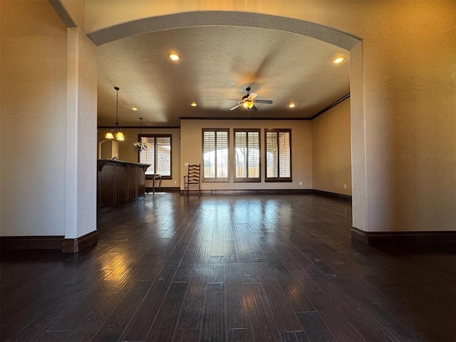 unfurnished living room featuring dark wood finished floors, crown molding, baseboards, and arched walkways