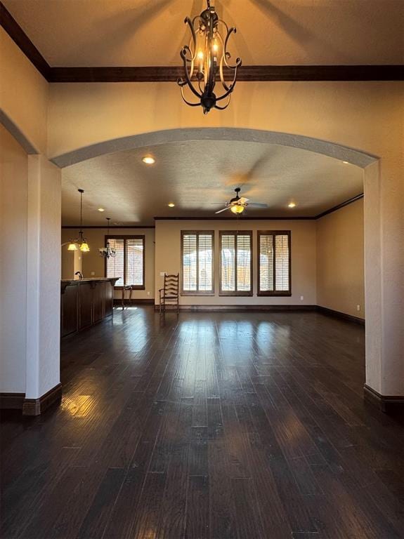 unfurnished living room featuring baseboards, ornamental molding, ceiling fan with notable chandelier, arched walkways, and dark wood-style flooring