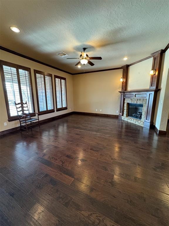 unfurnished living room with crown molding, ceiling fan, dark wood finished floors, a stone fireplace, and a textured ceiling