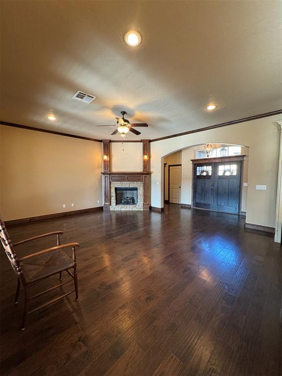 unfurnished living room featuring visible vents, arched walkways, wood finished floors, and ornamental molding