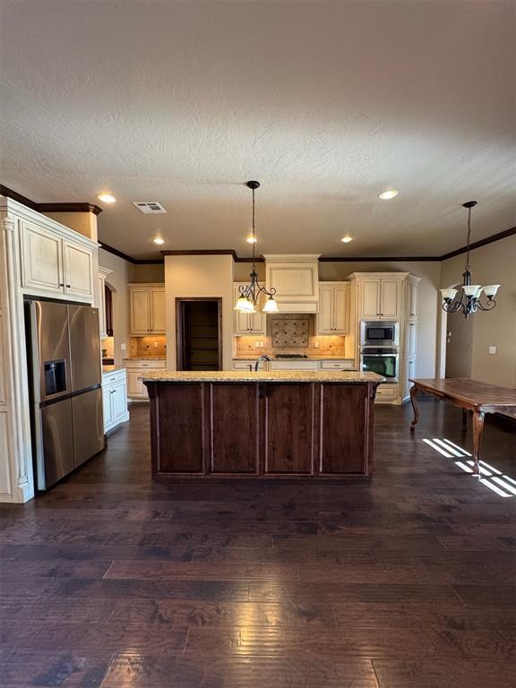 kitchen with ornamental molding, light stone counters, decorative backsplash, appliances with stainless steel finishes, and dark wood-style floors