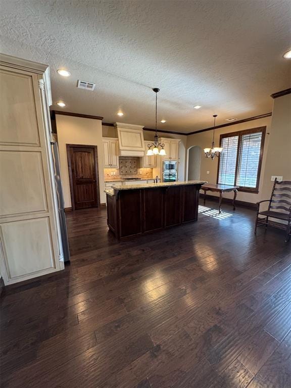 kitchen featuring visible vents, an island with sink, arched walkways, dark wood-style flooring, and stainless steel appliances