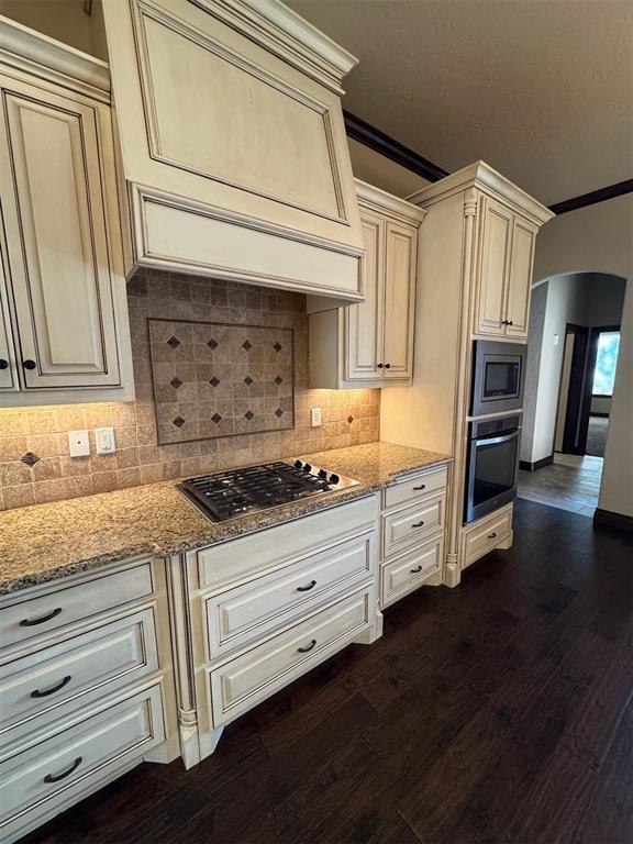 kitchen with light stone counters, cream cabinetry, arched walkways, and stainless steel appliances