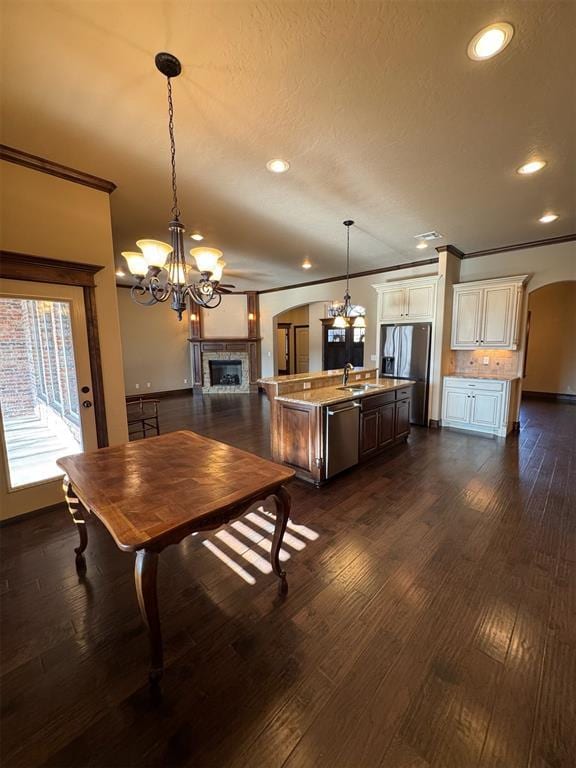 dining space featuring ornamental molding, dark wood finished floors, arched walkways, an inviting chandelier, and a fireplace