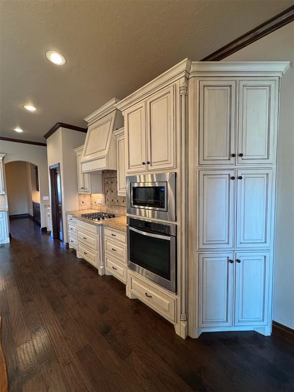 kitchen featuring backsplash, dark wood finished floors, custom exhaust hood, arched walkways, and stainless steel appliances