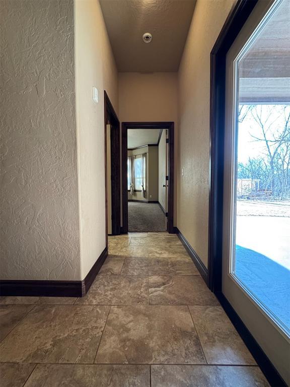 corridor featuring a healthy amount of sunlight, baseboards, and a textured wall