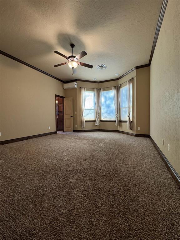 carpeted empty room featuring visible vents, a textured ceiling, crown molding, and a wall unit AC