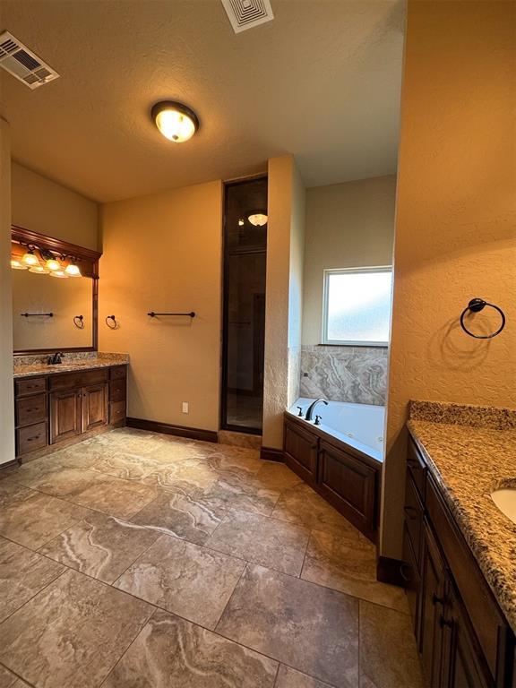 full bathroom with two vanities, a bath, and visible vents