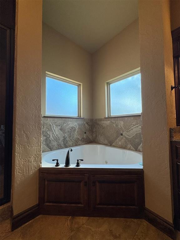 full bathroom with a jetted tub, vanity, baseboards, and a textured wall