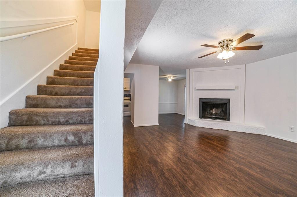 stairs featuring hardwood / wood-style floors, ceiling fan, a fireplace, and a textured ceiling