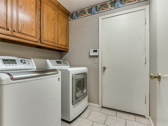 clothes washing area featuring washer and dryer, light tile patterned flooring, and cabinets