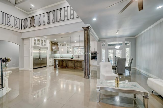 tiled living room with a high ceiling, french doors, crown molding, ceiling fan, and ornate columns