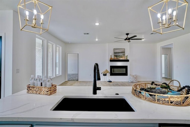 kitchen with sink, light stone counters, decorative light fixtures, light hardwood / wood-style flooring, and ceiling fan with notable chandelier