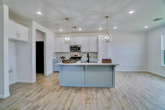 kitchen featuring hanging light fixtures, an island with sink, stainless steel appliances, decorative backsplash, and white cabinets