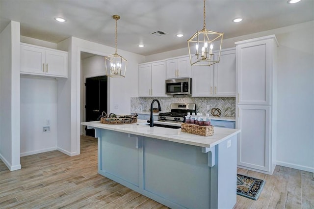 kitchen with pendant lighting, appliances with stainless steel finishes, white cabinets, a center island with sink, and decorative backsplash