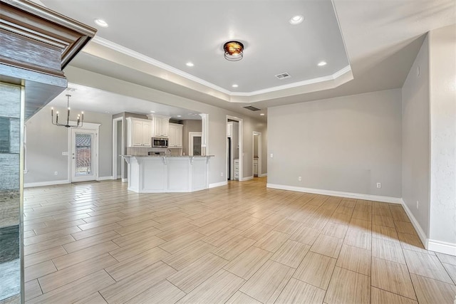 unfurnished living room with a raised ceiling, a notable chandelier, and ornamental molding