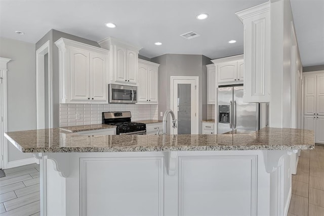 kitchen with decorative backsplash, light stone countertops, light wood-type flooring, appliances with stainless steel finishes, and white cabinetry