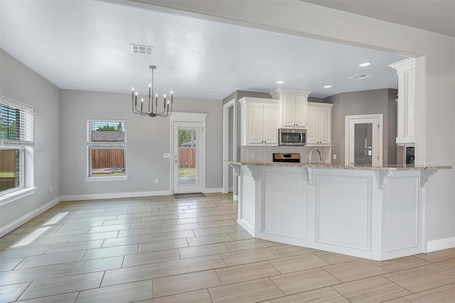 kitchen featuring light stone countertops, appliances with stainless steel finishes, kitchen peninsula, white cabinets, and a chandelier