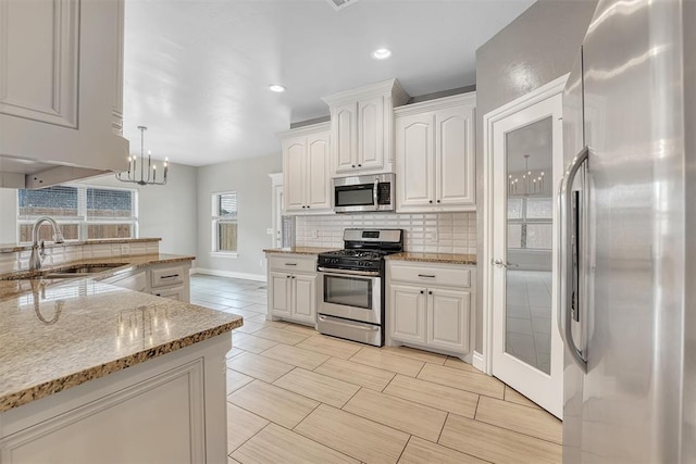 kitchen with appliances with stainless steel finishes, white cabinetry, hanging light fixtures, and sink