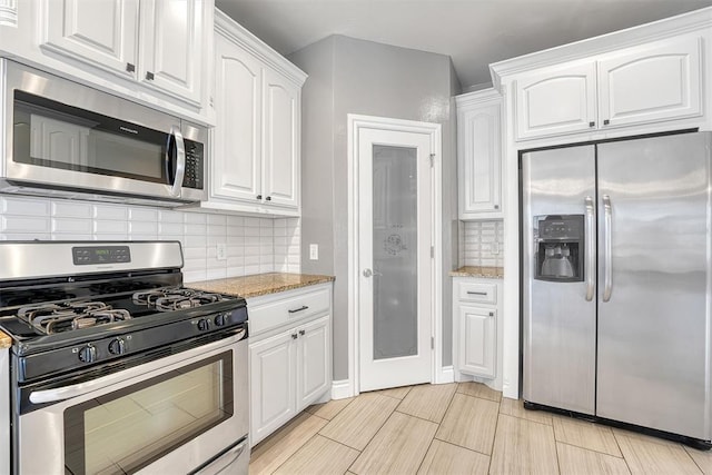 kitchen featuring backsplash, light stone countertops, white cabinets, and appliances with stainless steel finishes