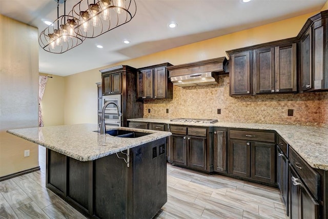 kitchen featuring wall chimney exhaust hood, a kitchen bar, sink, and a kitchen island with sink