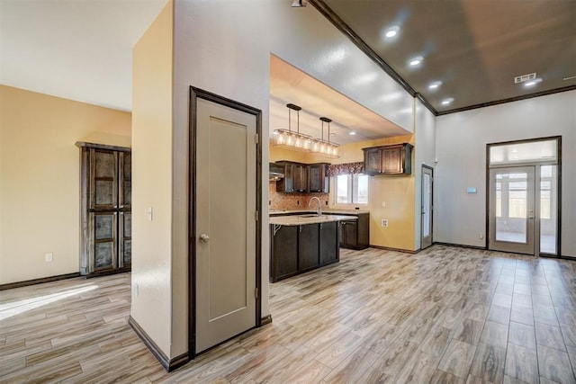 kitchen featuring backsplash, dark brown cabinets, a kitchen island with sink, sink, and hanging light fixtures