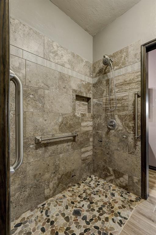 bathroom with a textured ceiling, wood-type flooring, and tiled shower