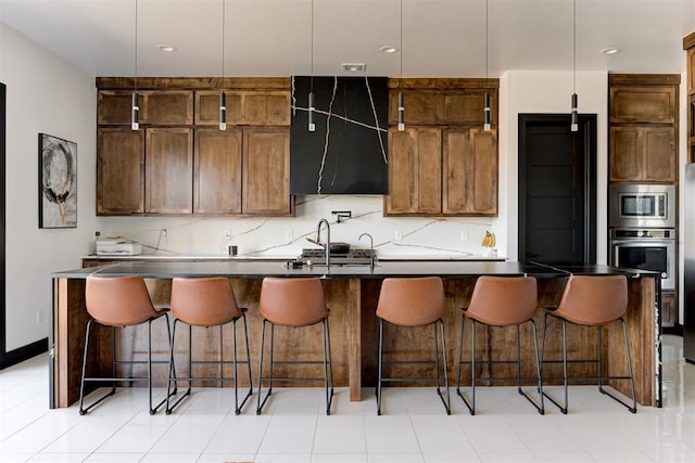 kitchen with a center island with sink, decorative backsplash, a kitchen bar, and stainless steel appliances