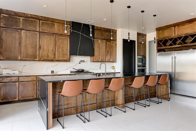 kitchen with appliances with stainless steel finishes, backsplash, ventilation hood, a center island with sink, and hanging light fixtures