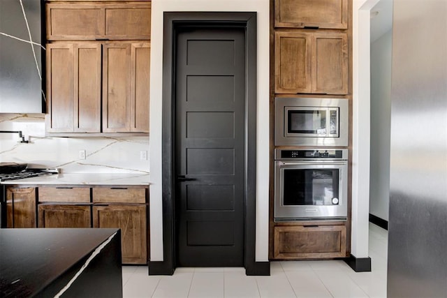 kitchen featuring light stone countertops, appliances with stainless steel finishes, tasteful backsplash, and light tile patterned floors