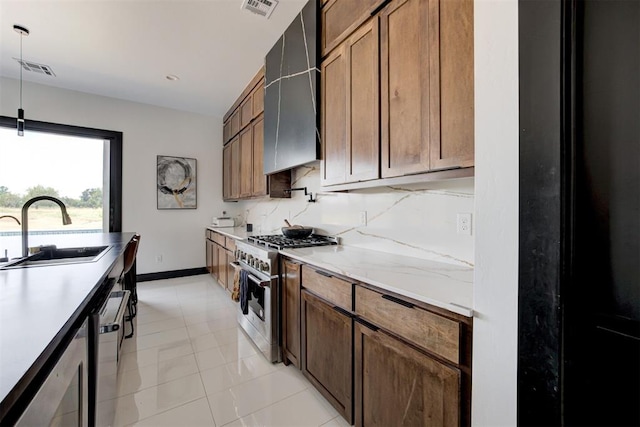 kitchen featuring appliances with stainless steel finishes, wall chimney range hood, sink, light tile patterned floors, and hanging light fixtures