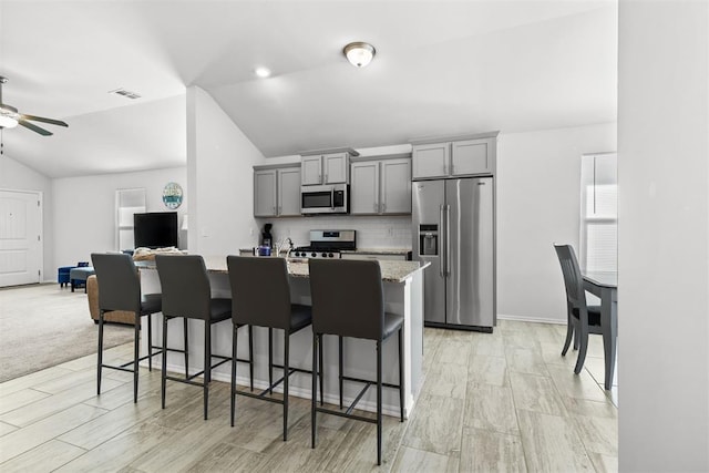 kitchen with visible vents, stainless steel appliances, a breakfast bar area, and gray cabinetry